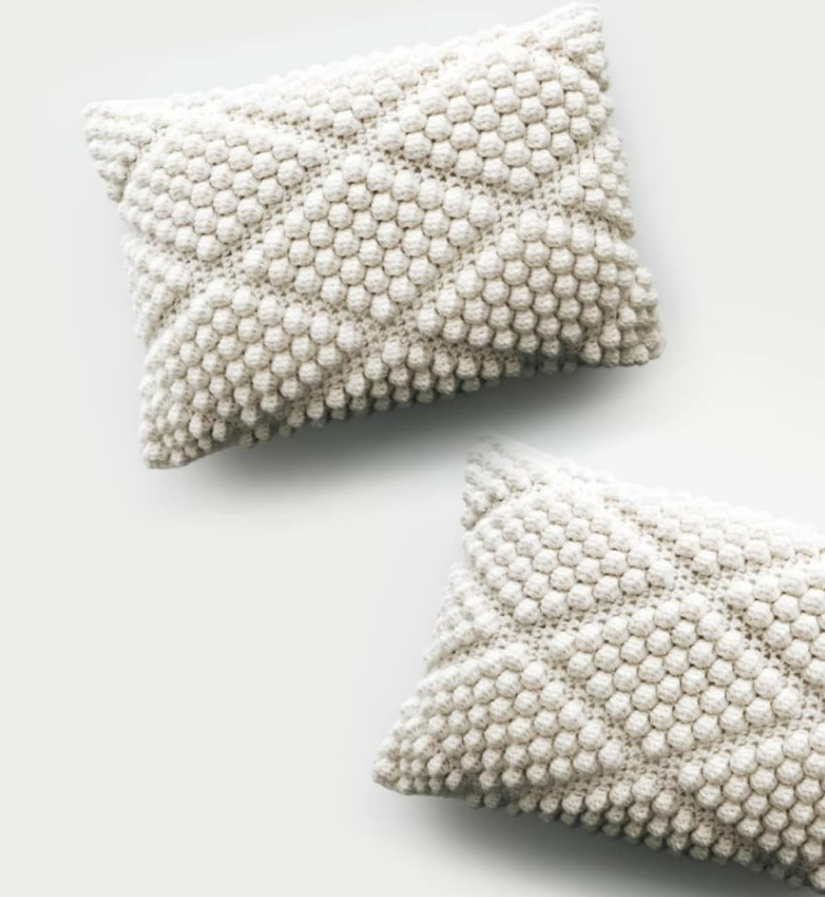 Two cream crochet cushions with a diamond bobbled pattern all over them on a white background.
