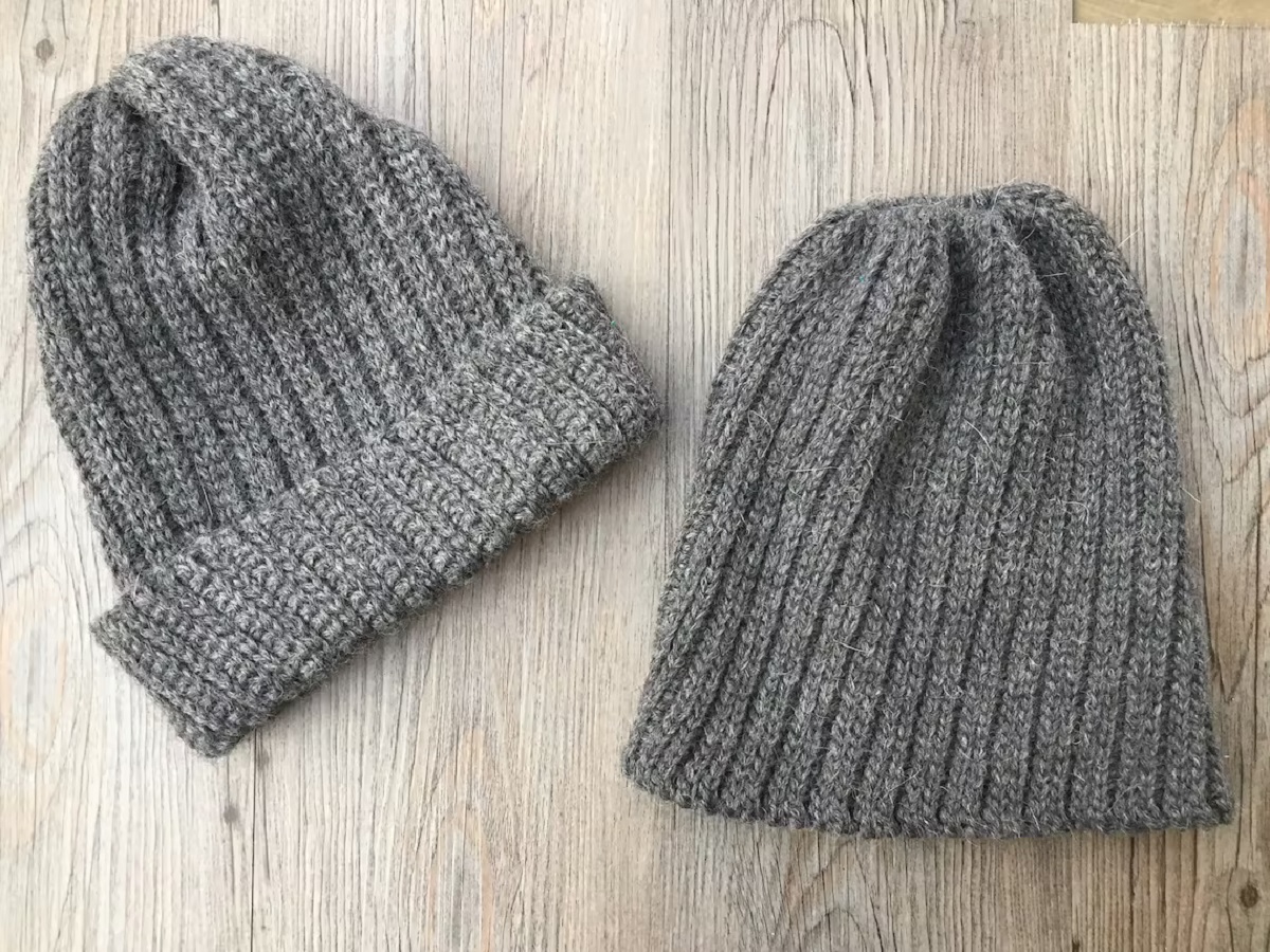 Two gray ribbed crochet beanies lying next to each other on a wooden floor, one with a banding across the bottom and one without.
