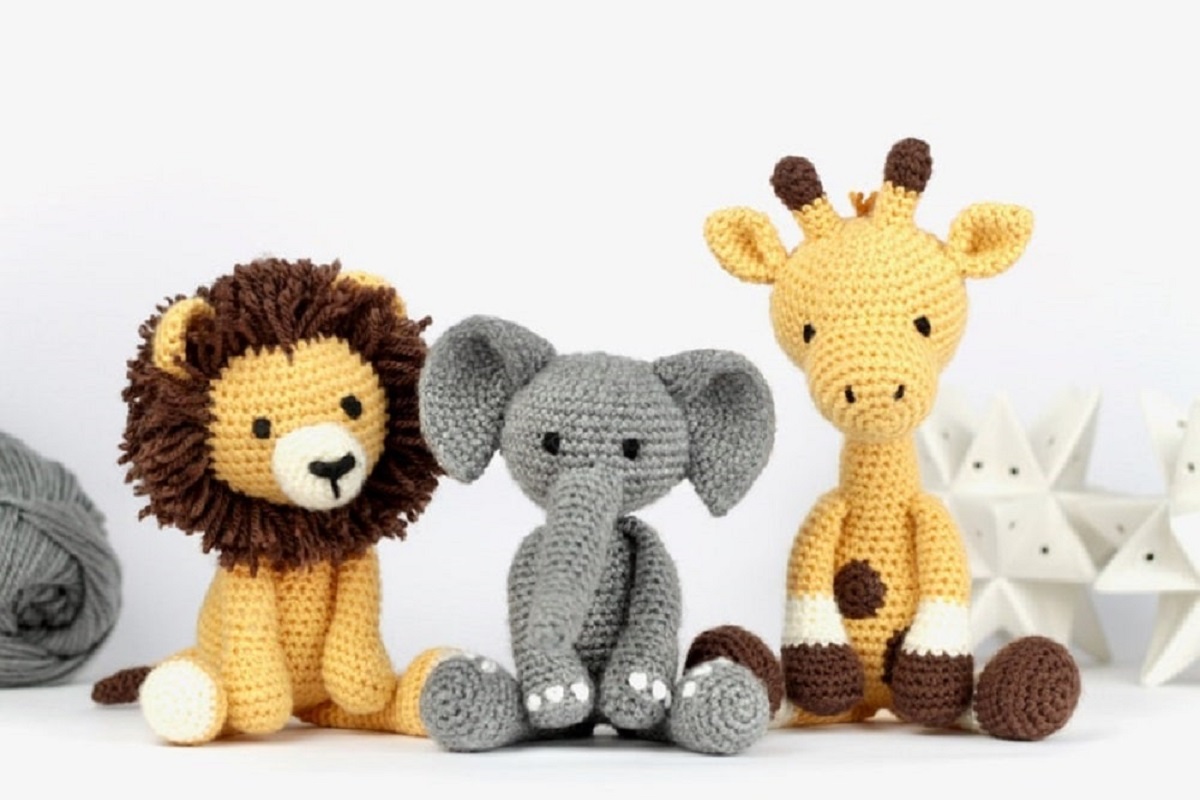 A yellow crochet lion with a brown mane next to a gray elephant and a yellow and brown giraffe.