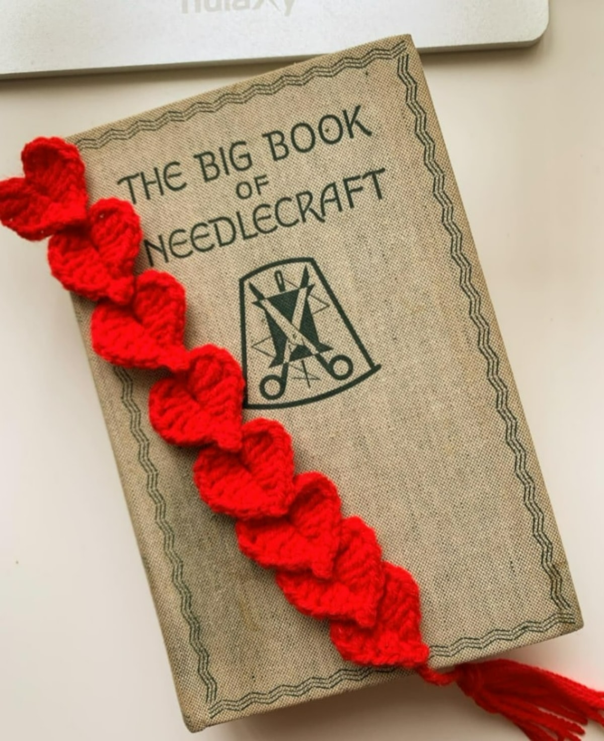 Red crochet hearts linked together to create a bookmark with a red tassel at the bottom on top of a brown book.
