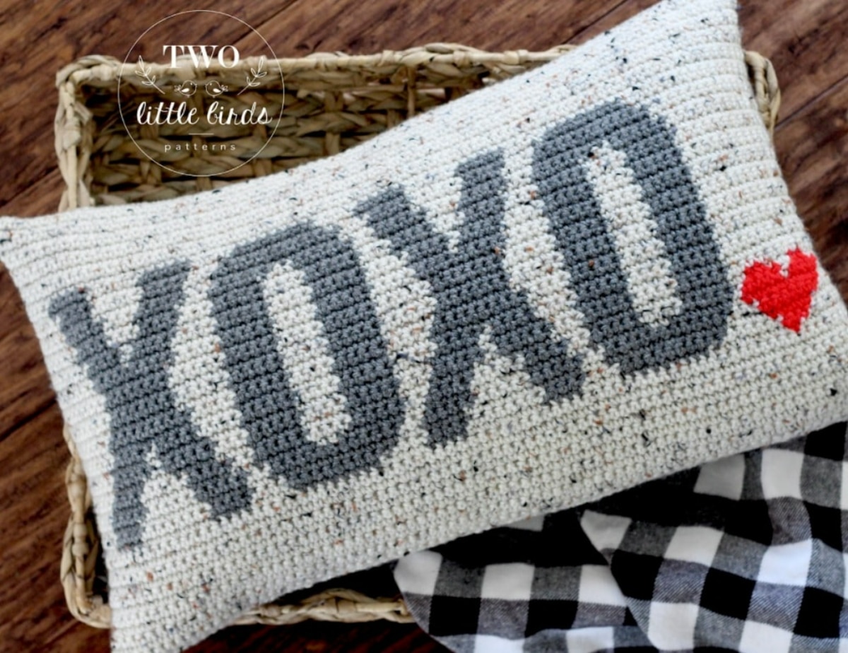 Cream crochet cushion with blue speckles throughout and ‘XOXO’ written across it with a small red heart in the bottom right corner.